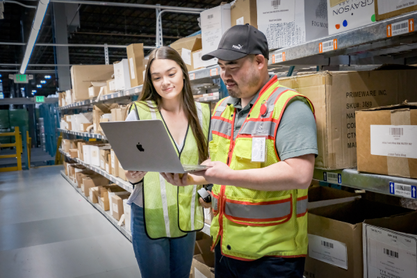 A WineDirect employee with a customer in the fulfillment warehouse happily looking at an iPad.